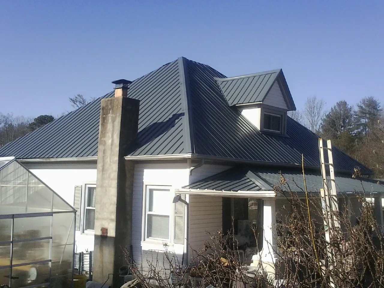 Dark blue standing seam metal roof on a white farmhouse with dormer — Slate & Tile Roof Repair by Roofing Brothers in Mckenna