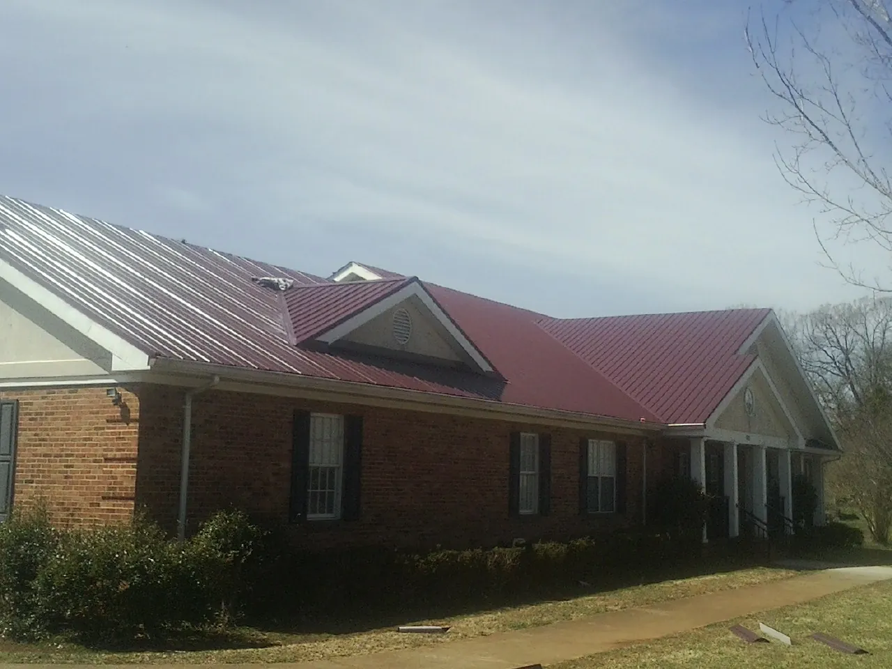 Red metal roof with gabled entries on a long brick building, from a Hail Damage Roof Repair job in Mckenna