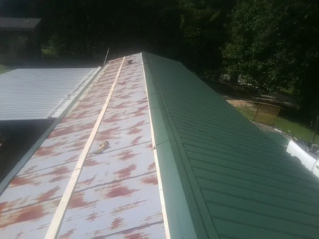 Old rusted panels beside newly installed green metal roofing — Wind Damage Roof Repair by Roofing Brothers in Mckenna