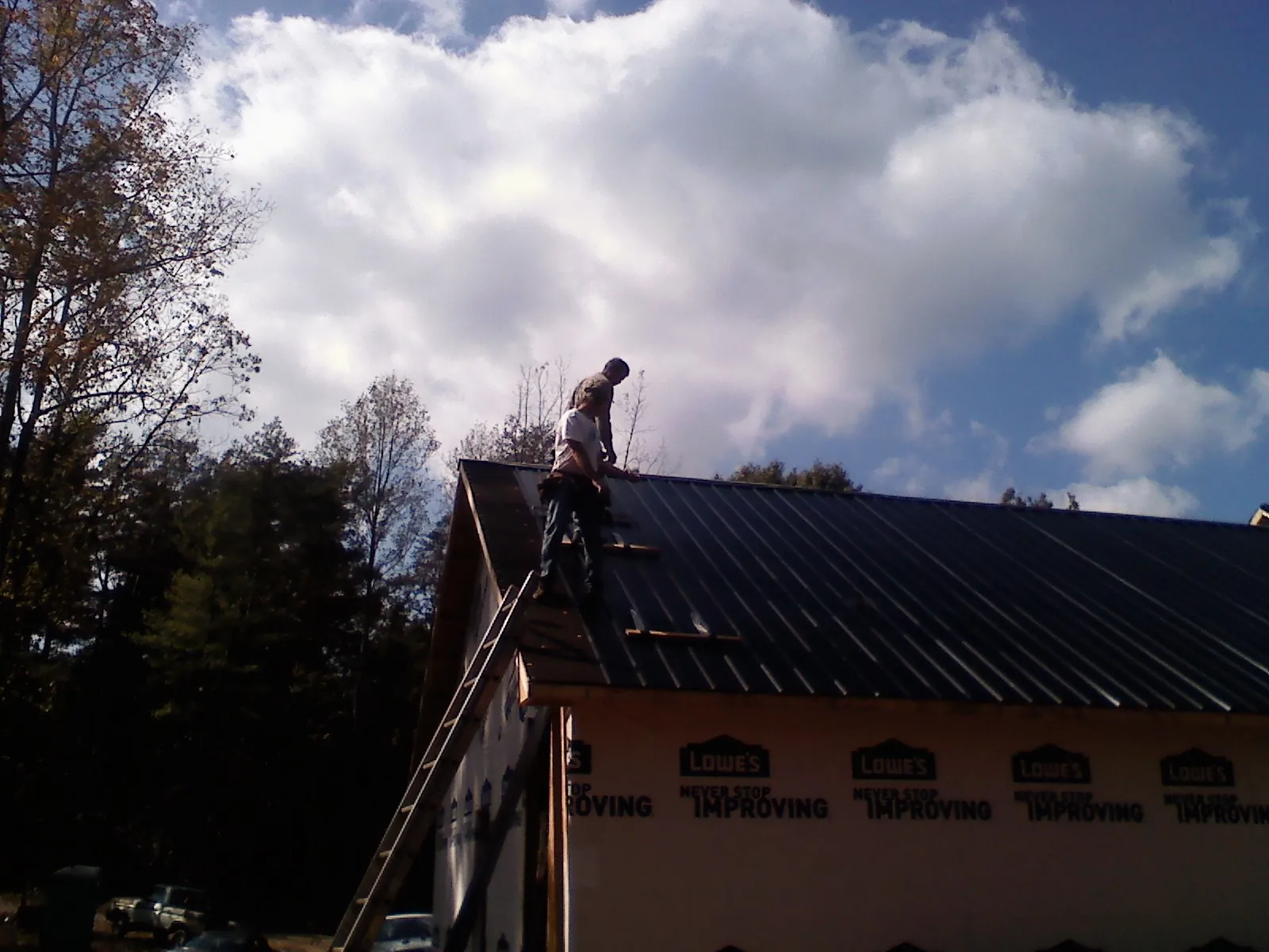 Roofer fastening dark metal panels high against a cloudy sky, from a Roof Inspection job in Mckenna