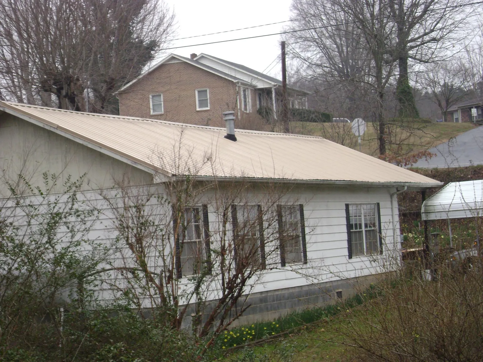 Tan metal roof on a white sided house set into a hillside — Commercial Roofing by Roofing Brothers in Mckenna
