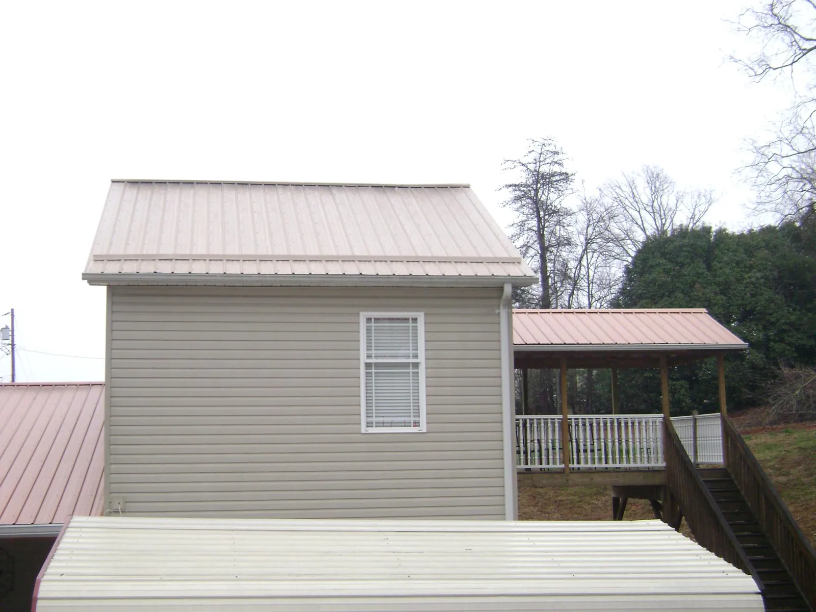 Tan metal roofs on a two story addition and attached porch, from a Roof Replacement job in Mckenna